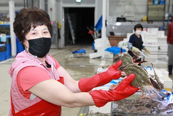 수산동 상인이 게 두마리를 들고 카메라를 바라보고 있다. [사진=새수원신문]